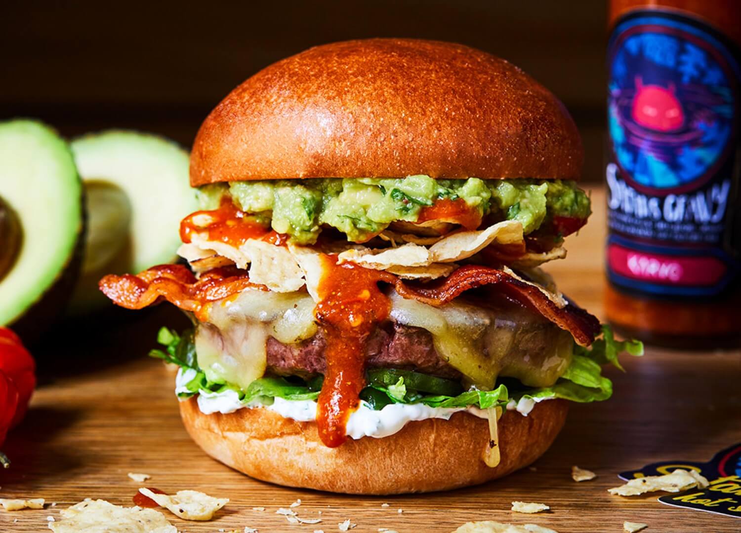 Honest beef burger with hot sauce, bacon, cheese, avocado and nachos
